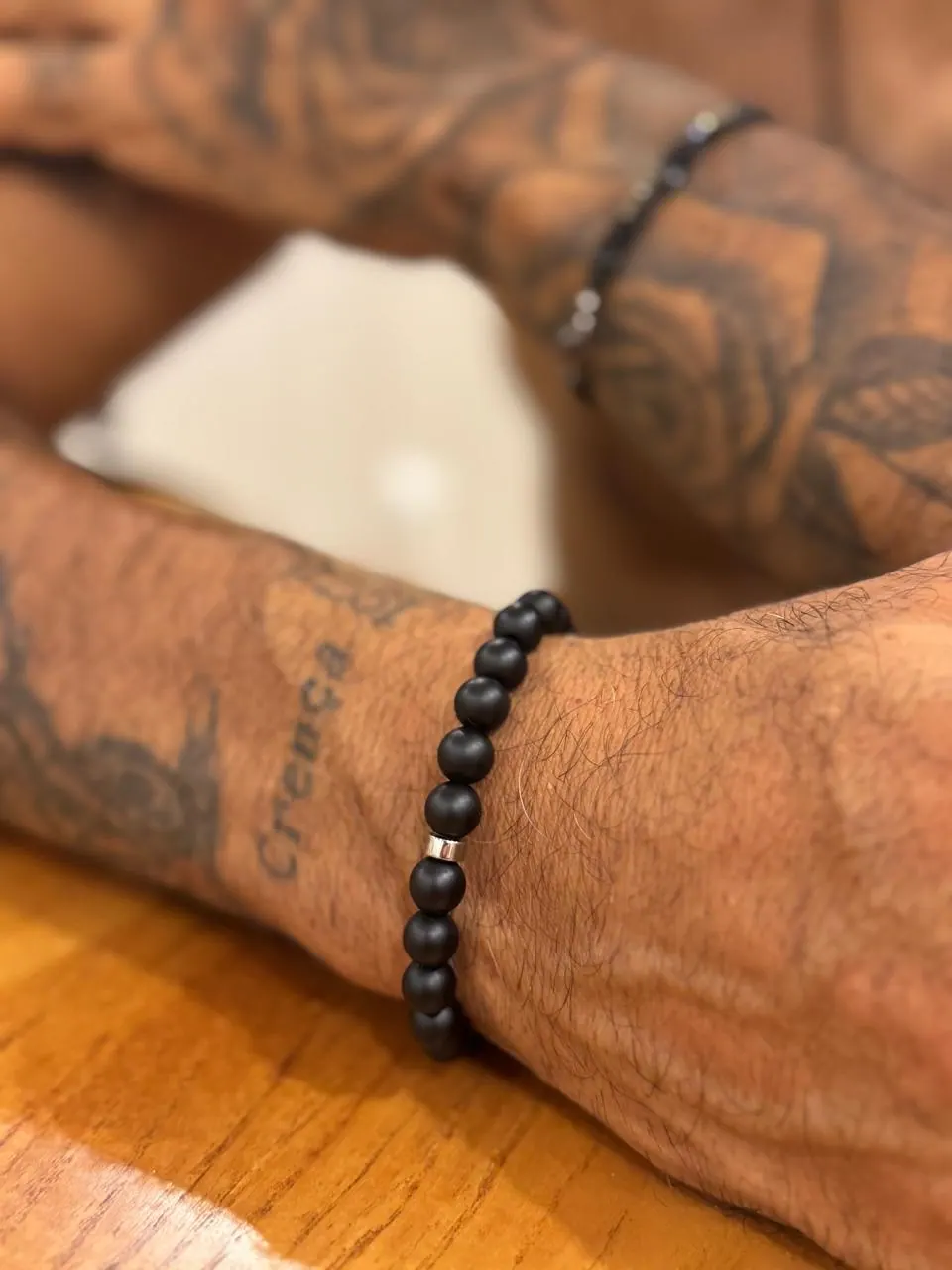 Pulseira Basalto em ônix fosco no pulso, apoiado numa mesa de madeira